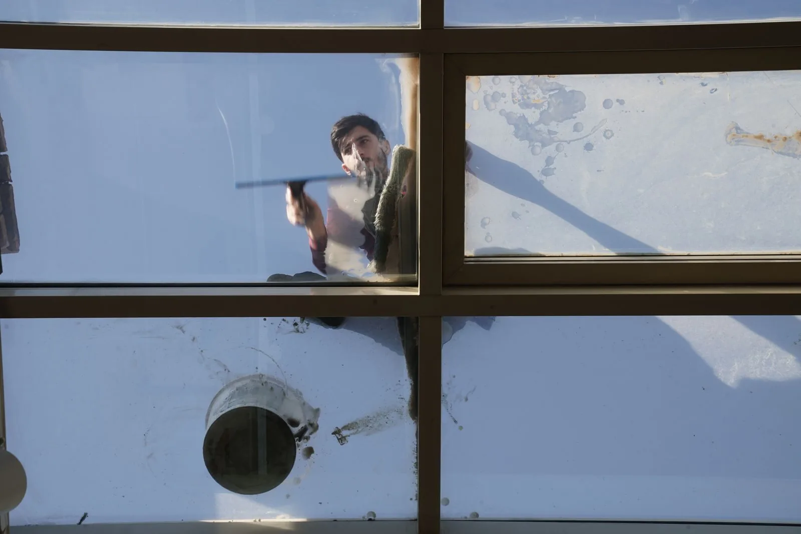 Window cleaner using a squeegee on glass against a blue sky