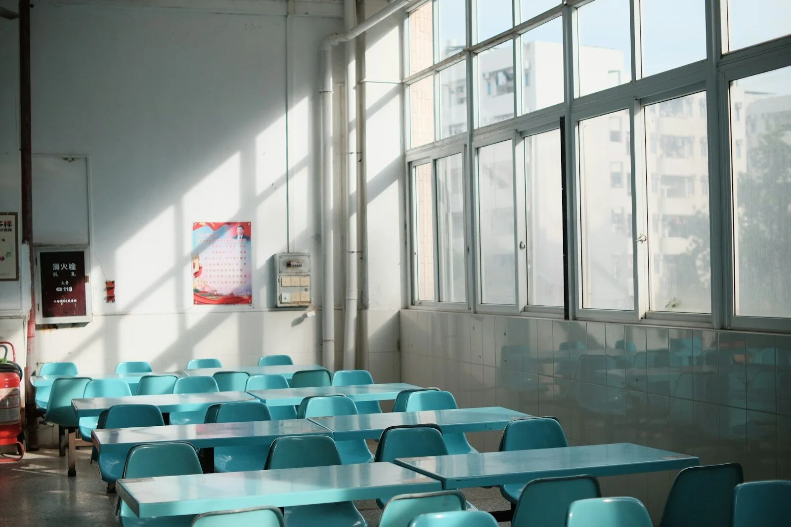 Empty school canteen with tables, teal chairs and tall windows
