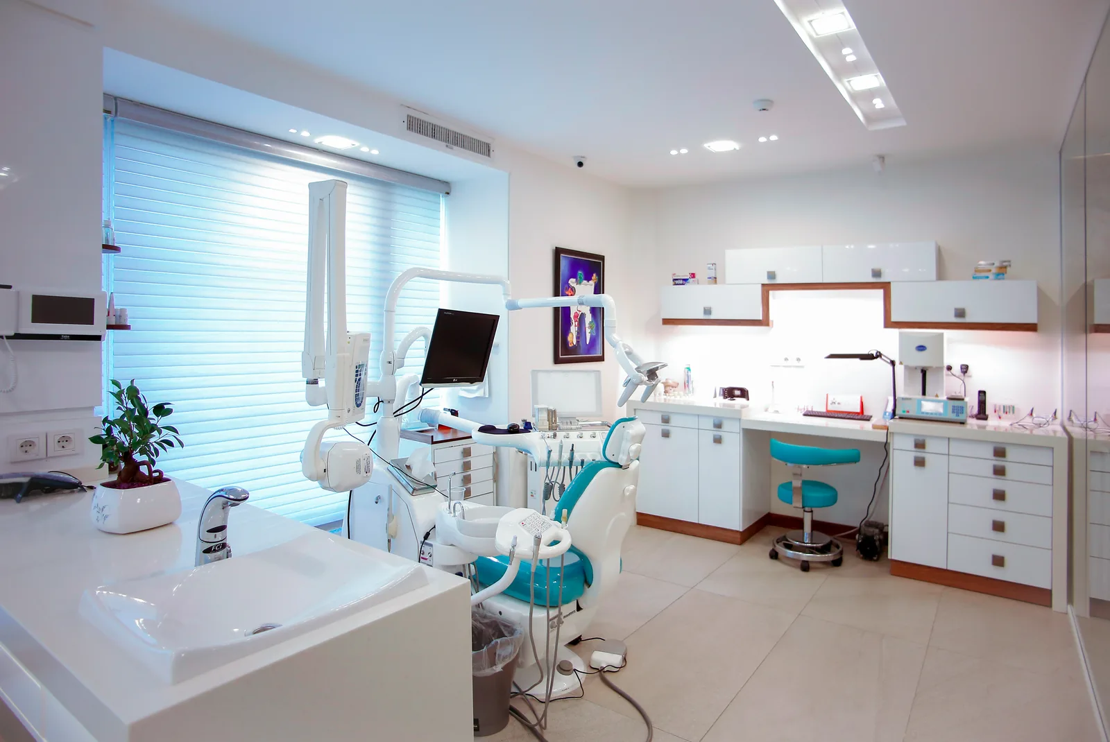 Bright dental treatment room with a patient chair, sink and white cabinets