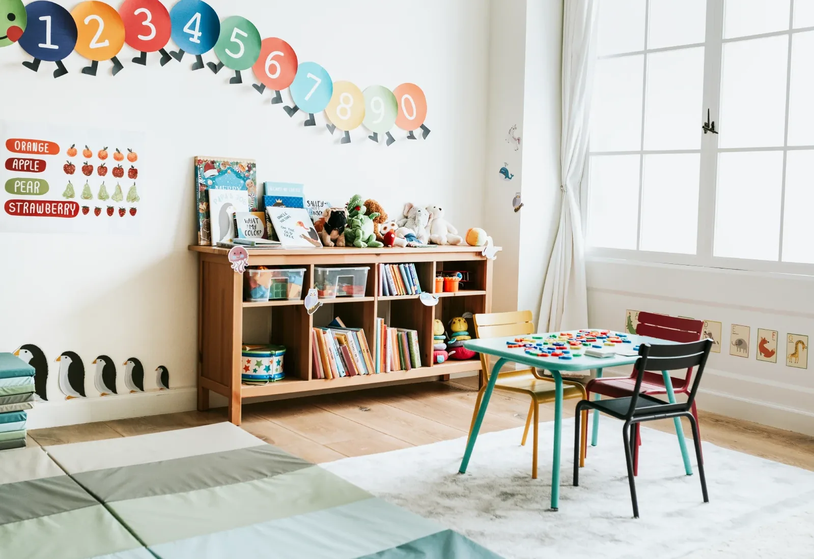 Child care playroom with a bookshelf of toys, a small table and colourful chairs