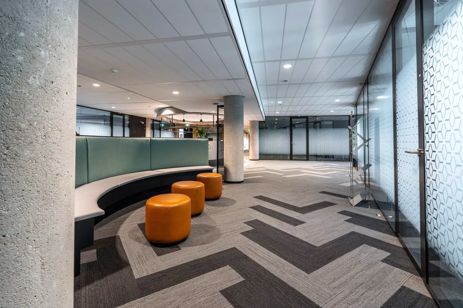 Clean office breakout area with orange stools and patterned carpet