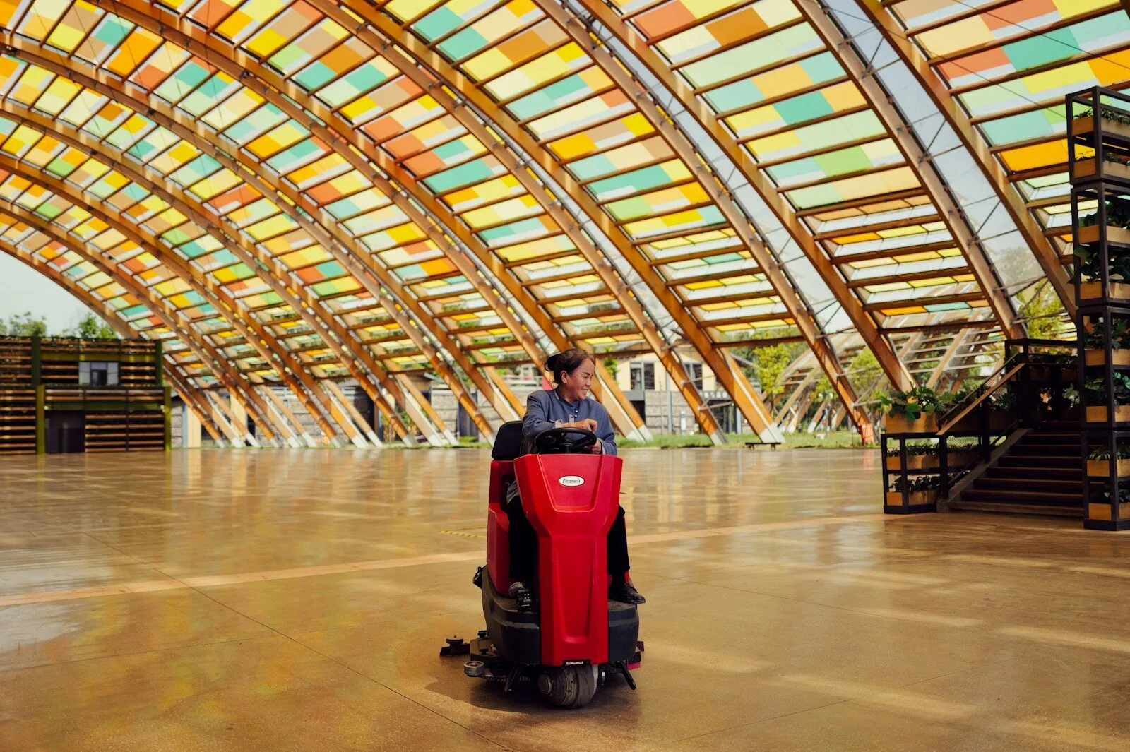 Cleaner driving a ride-on floor scrubber across a large polished floor